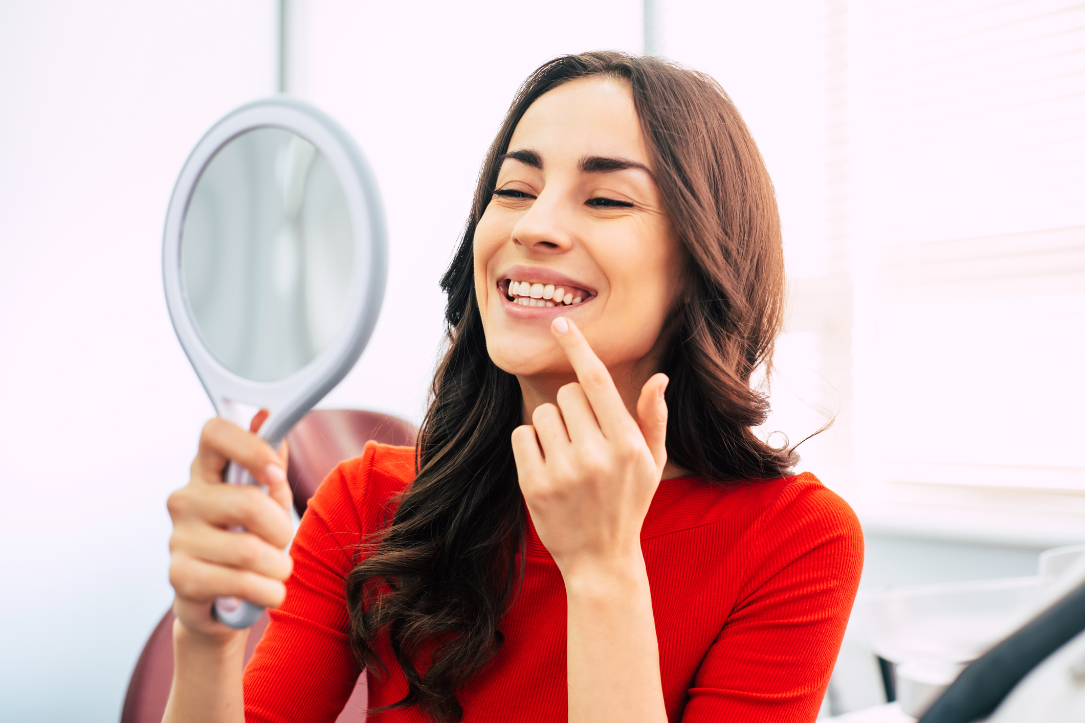woman looking a teeth in hand held mirror